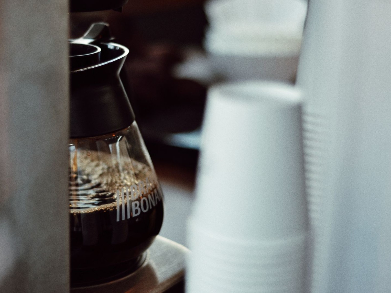 A drip coffee carafe next to cups ready to serve
