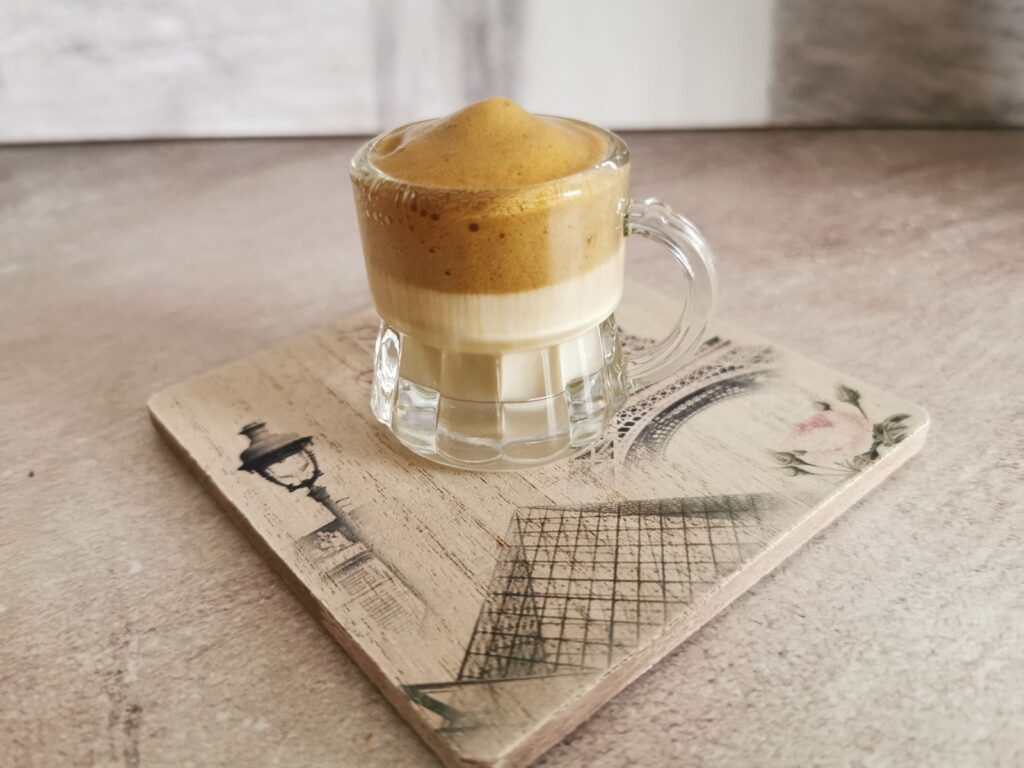 Whipped dalgona coffee with thick foam on a wooden coaster