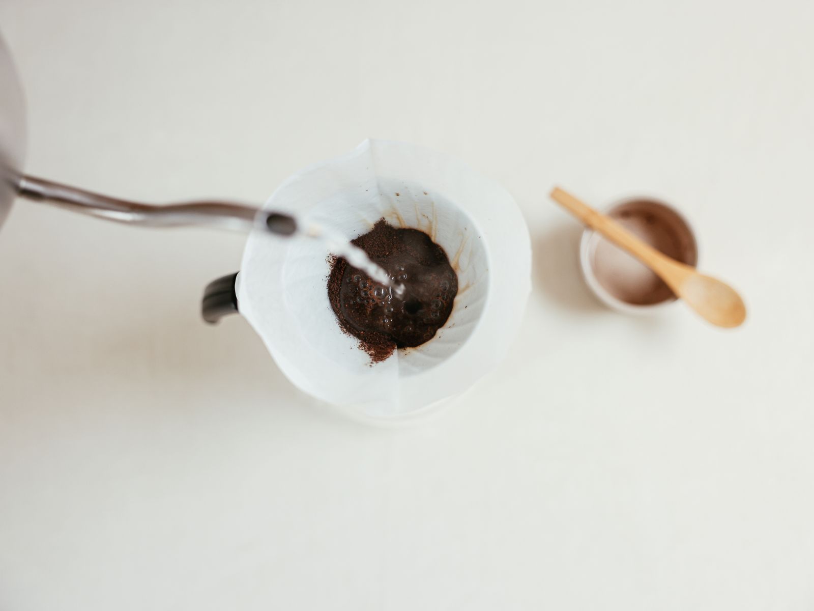 Close-up of a gooseneck kettle pouring a thin stream over a pour-over filter