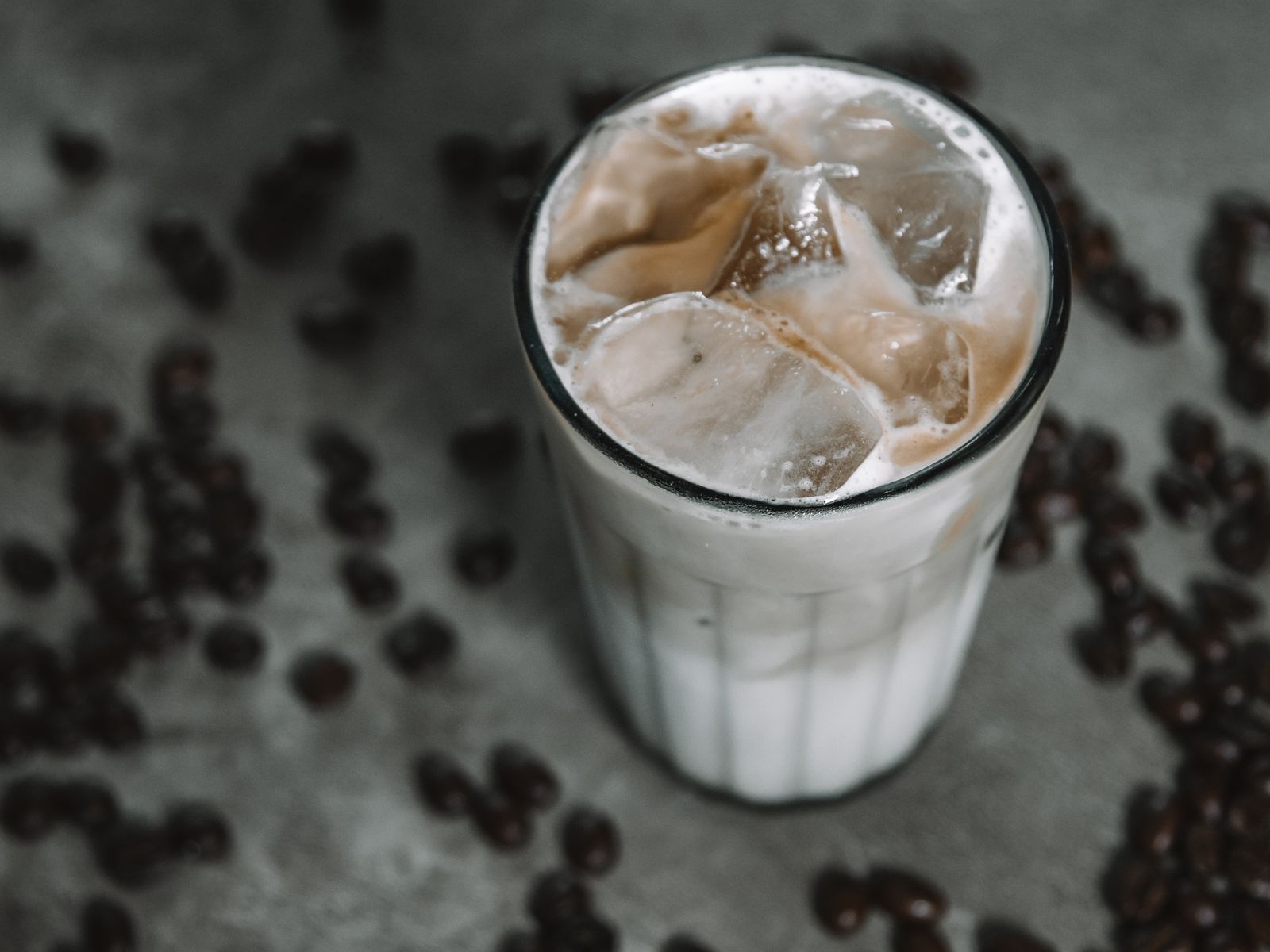 Creamy iced coffee over ice cubes surrounded by coffee beans