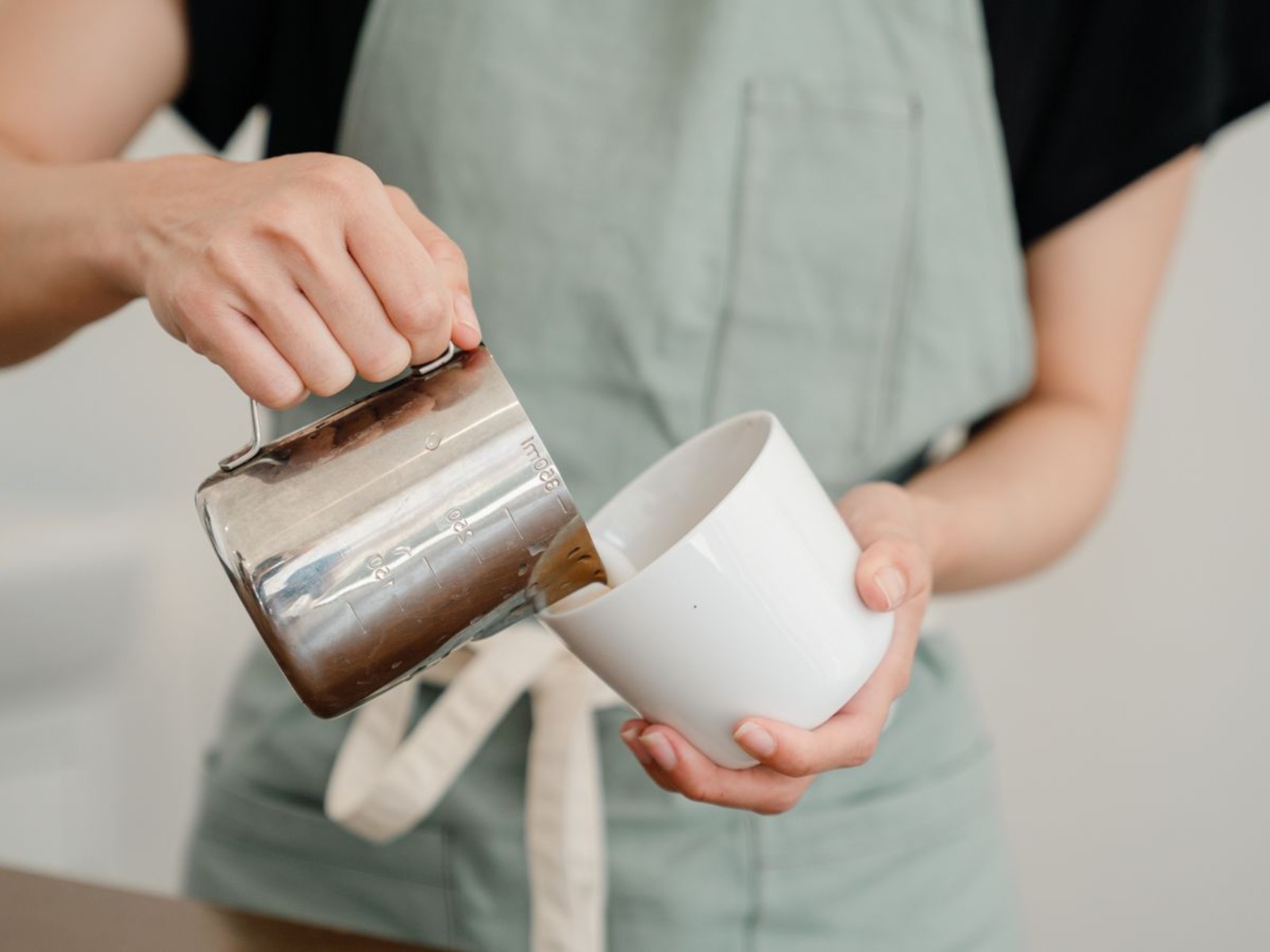 Pouring milk from a steel pitcher to make latte art