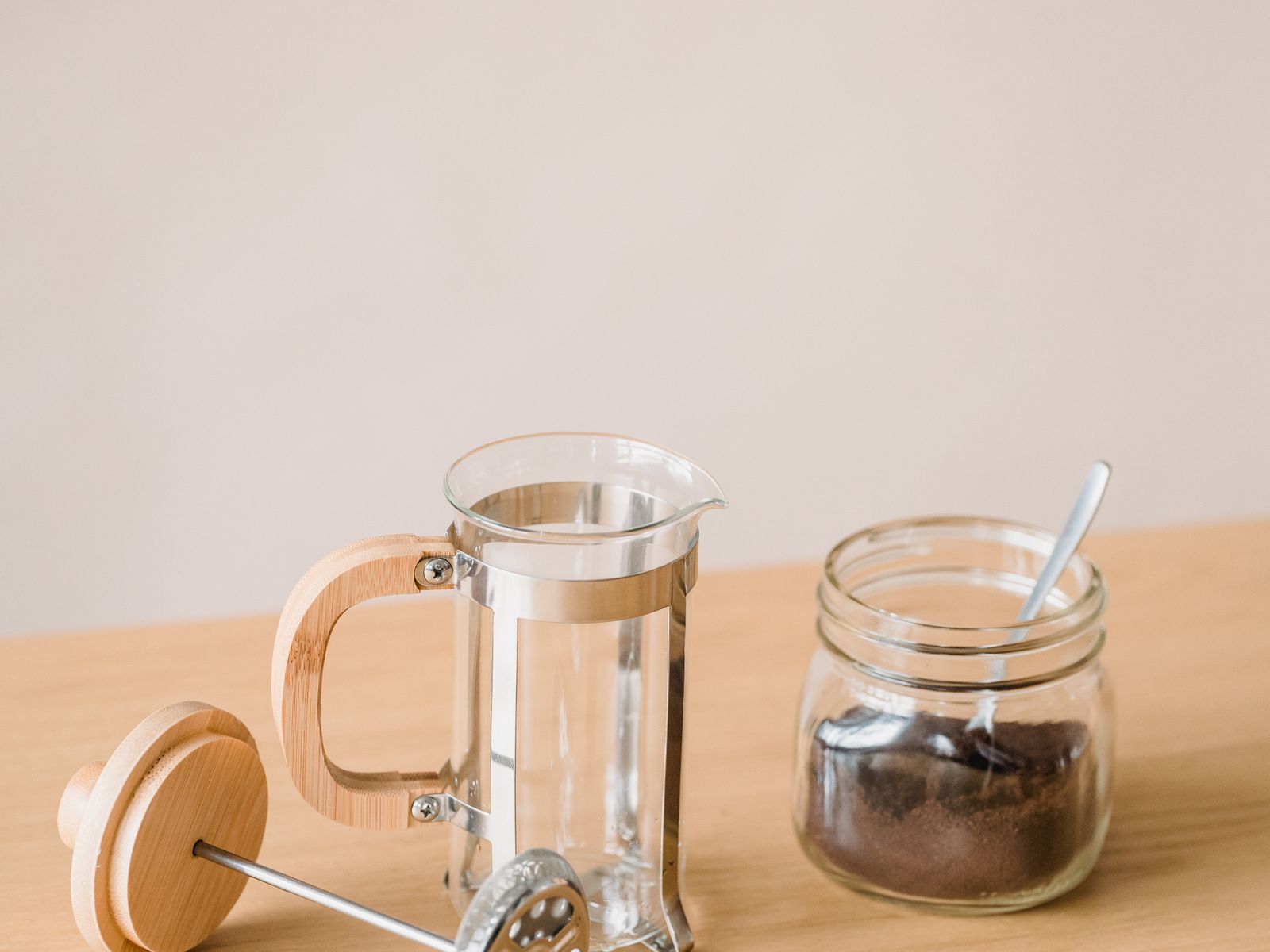 Minimalist French press and coffee jar on a wooden surface