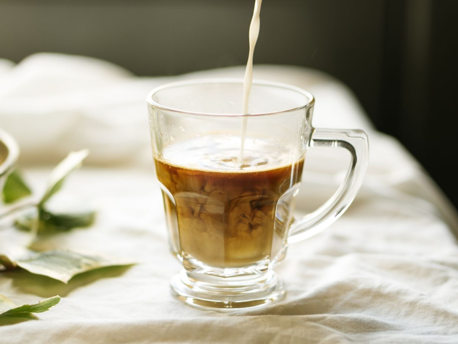 Plant-based milk being poured into a glass of coffee