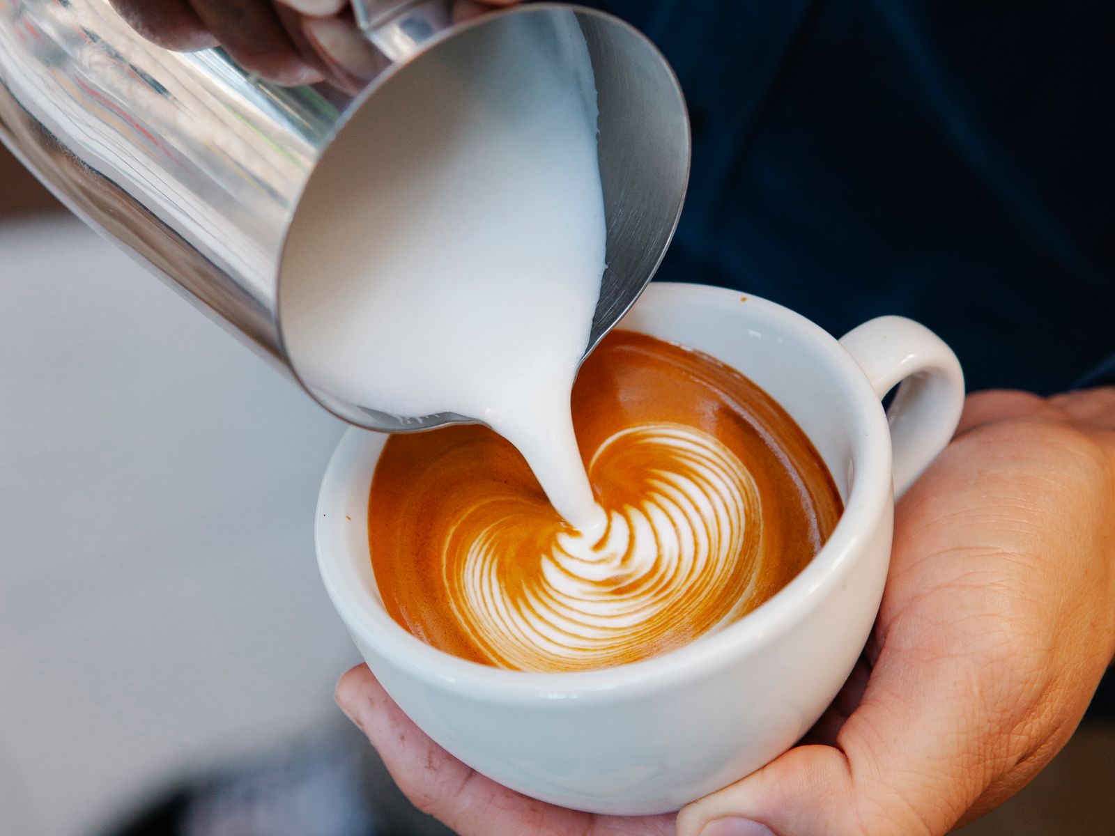 Barista wiggling the pitcher to pour a rosetta into a cup