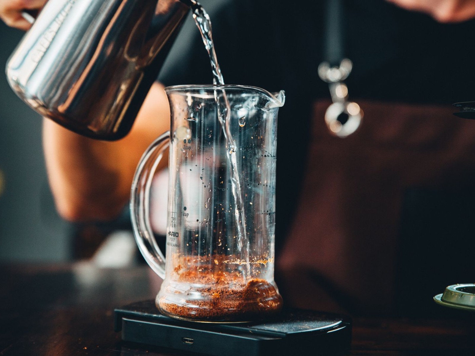 Hands pouring hot water over coffee grounds in a glass brewer