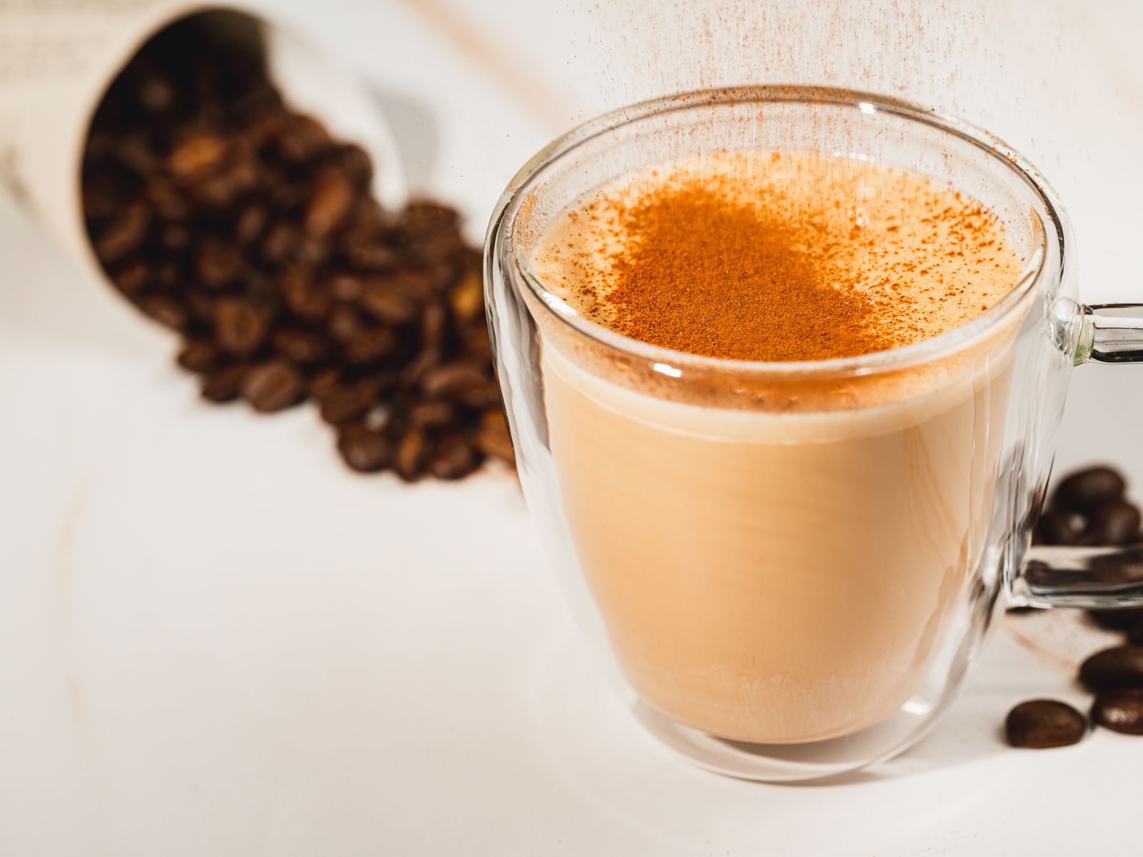 A warm pumpkin spice latte topped with cinnamon and surrounded by coffee beans