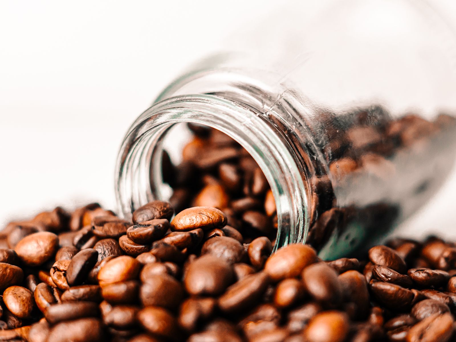 Roasted coffee beans spilling out of a glass jar