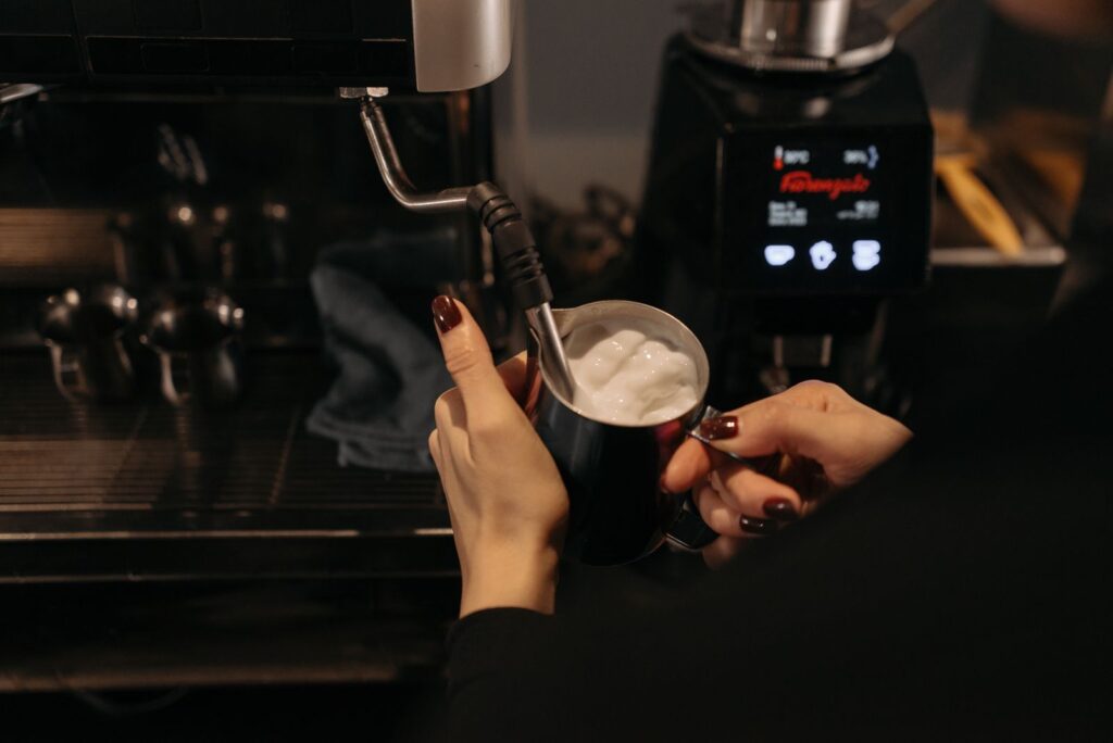 A barista using a steam wand to steam milk for microfoam