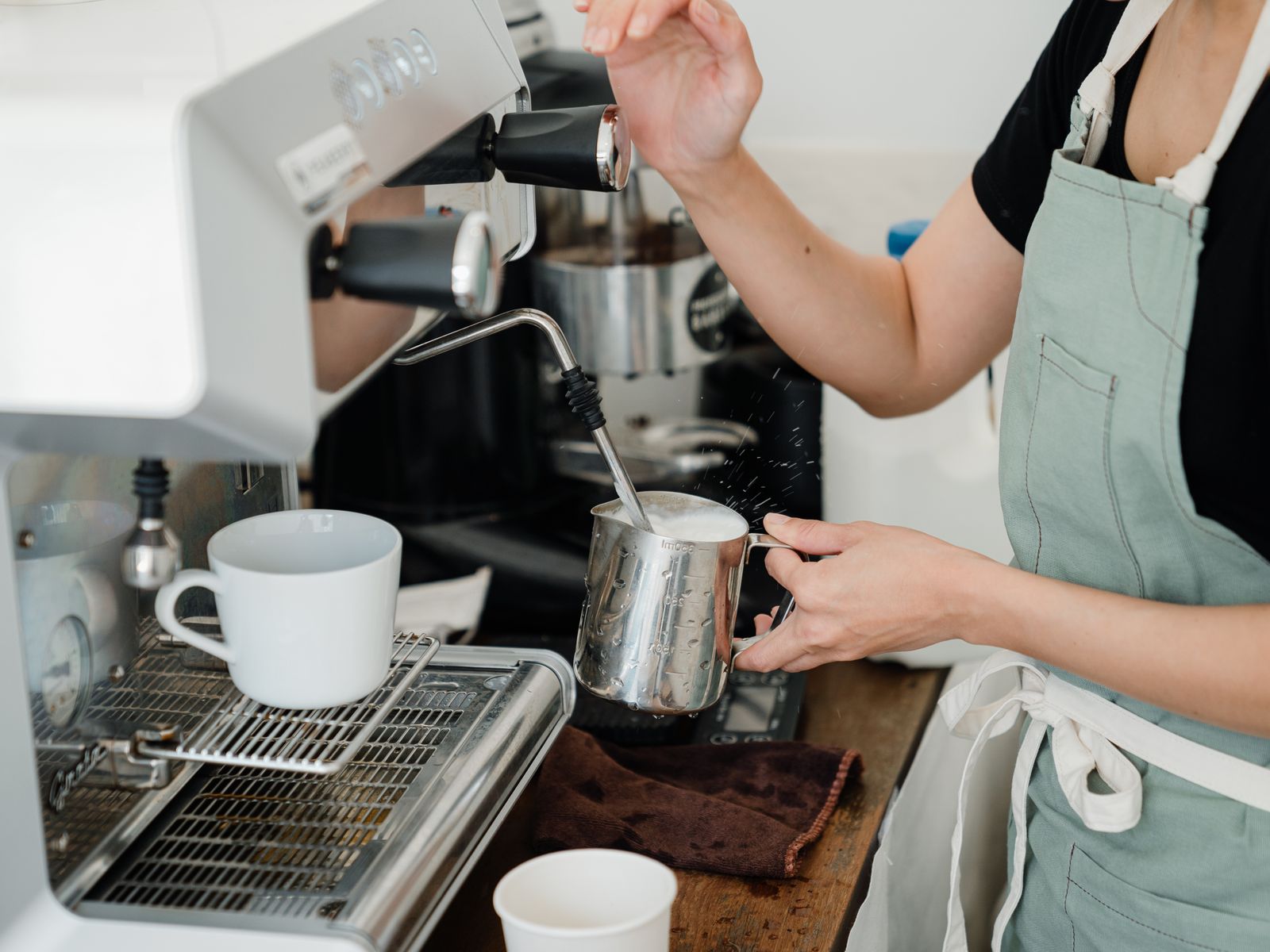 Barista steaming milk in a stainless steel pitcher on an espresso machine