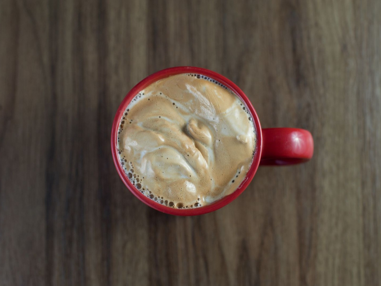 Overhead view of whipped coffee foam layered over milk in a red mug