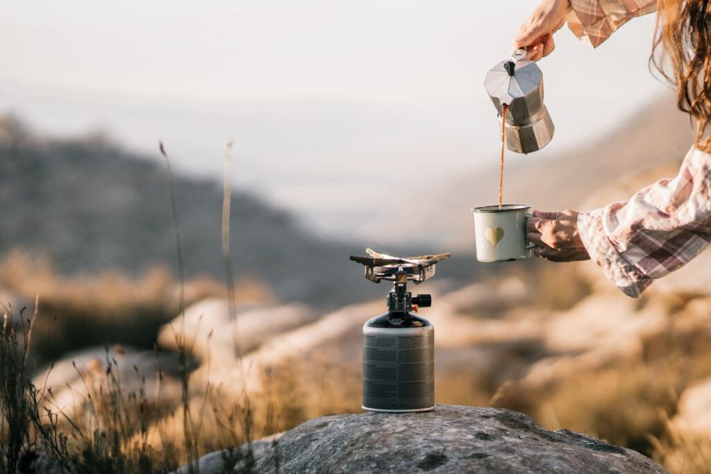 Pouring coffee from a moka pot to brew coffee while camping on a stove