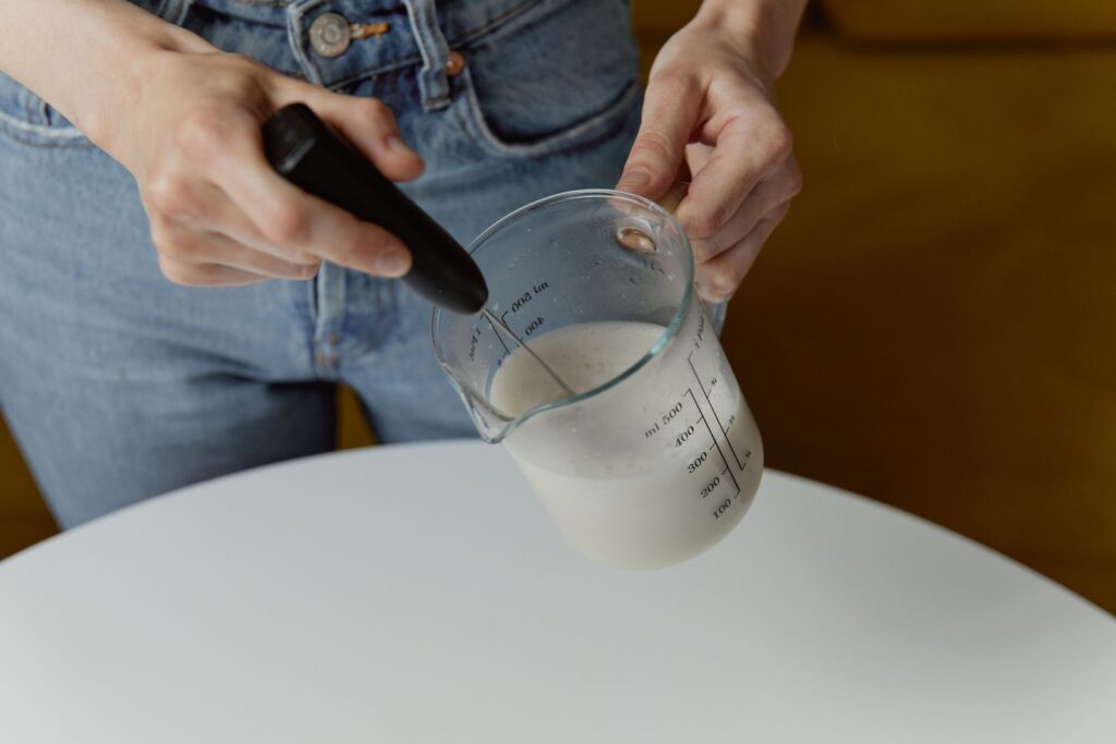 A handheld milk frother frothing milk, ready to clean your milk frother after use
