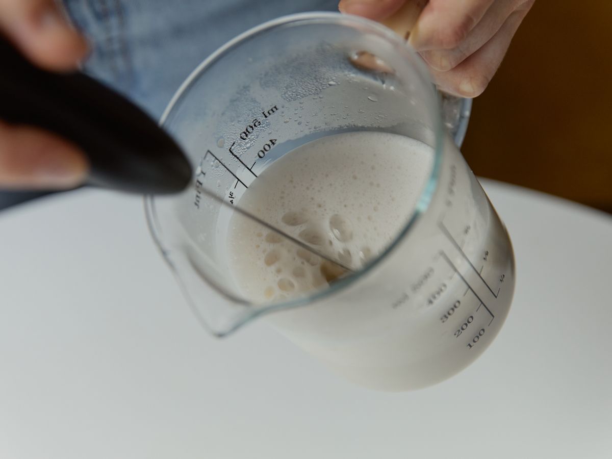 Milk being frothed in a glass measuring cup with a handheld frother