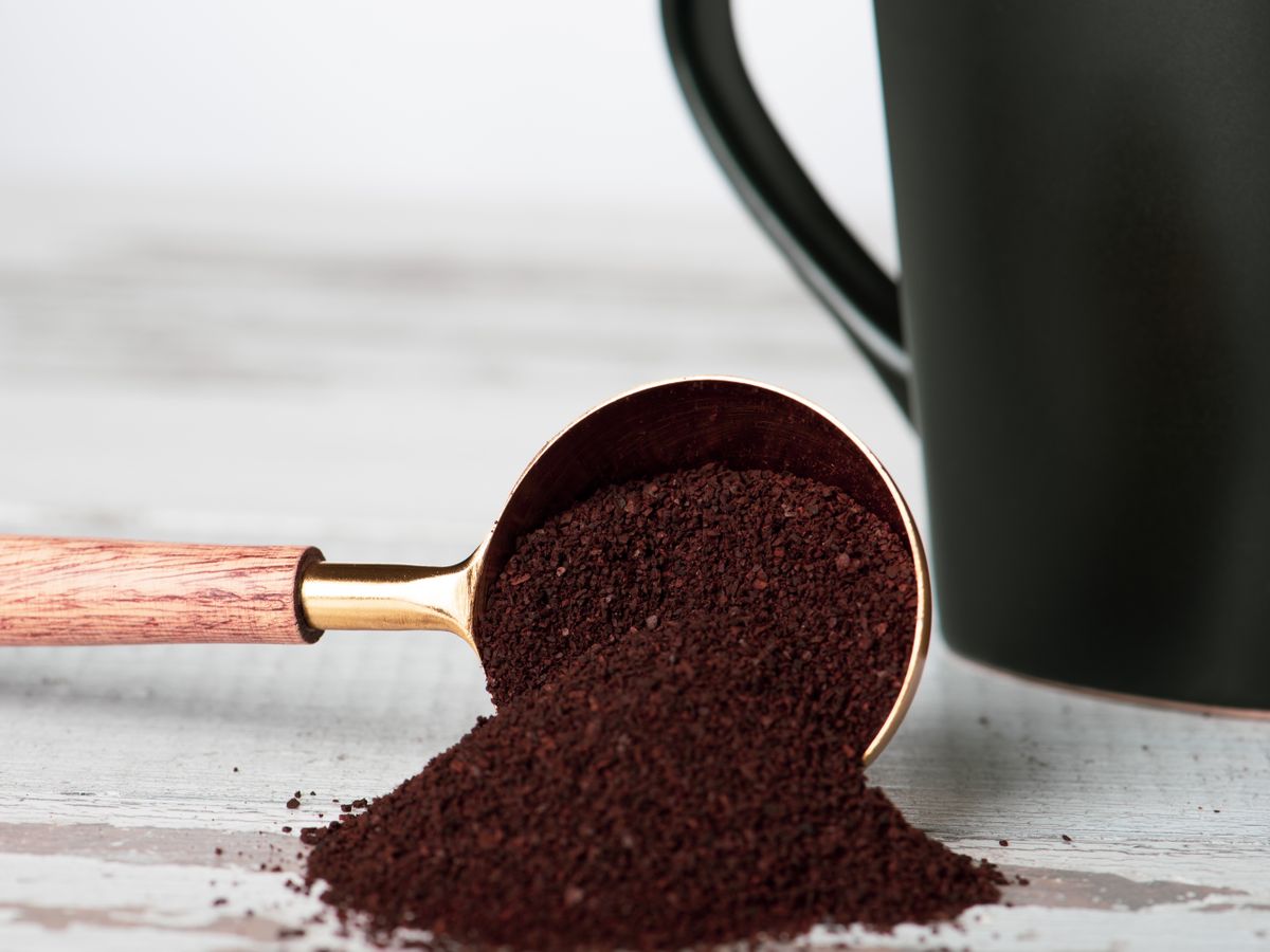 Freshly ground coffee spilling from a scoop beside beans