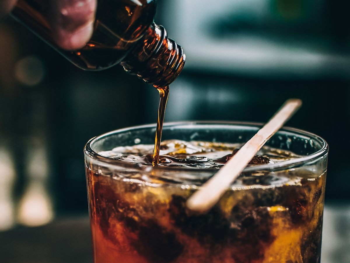 Dark homemade coffee syrups poured into an iced coffee with a wooden stirrer