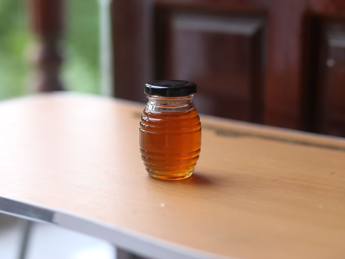 A glass jar of amber homemade syrup stored on a wooden table