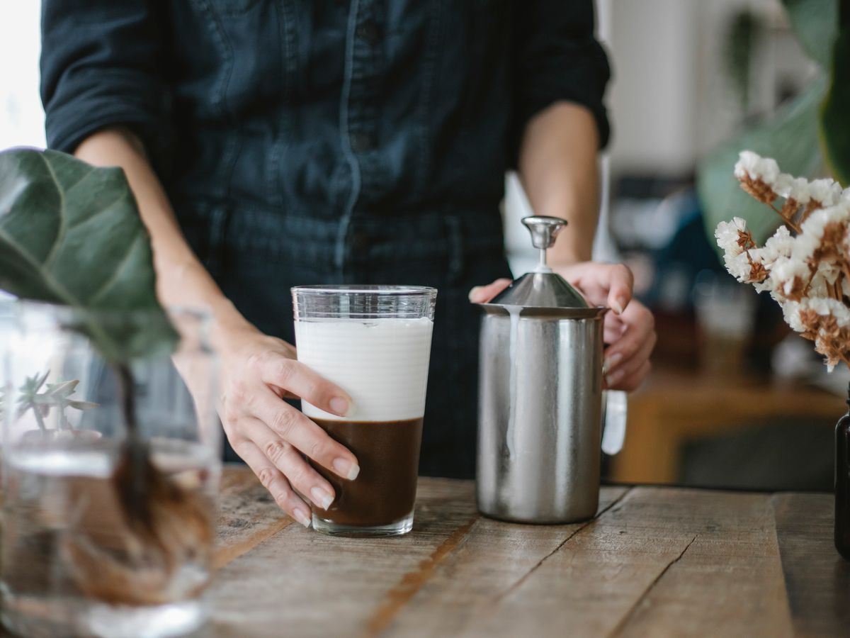 Hands using a manual stainless steel milk frother pitcher