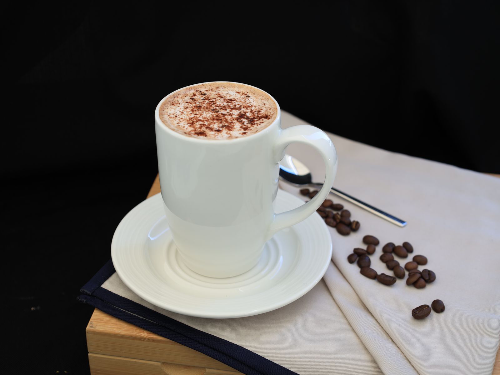 Finished mocha in a white cup dusted with cocoa beside coffee beans