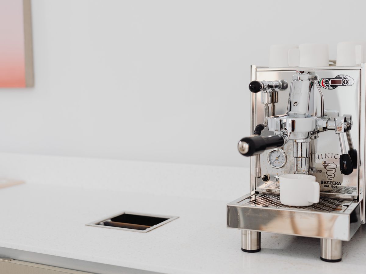 A sleek stainless steel espresso machine with cups in a bright kitchen