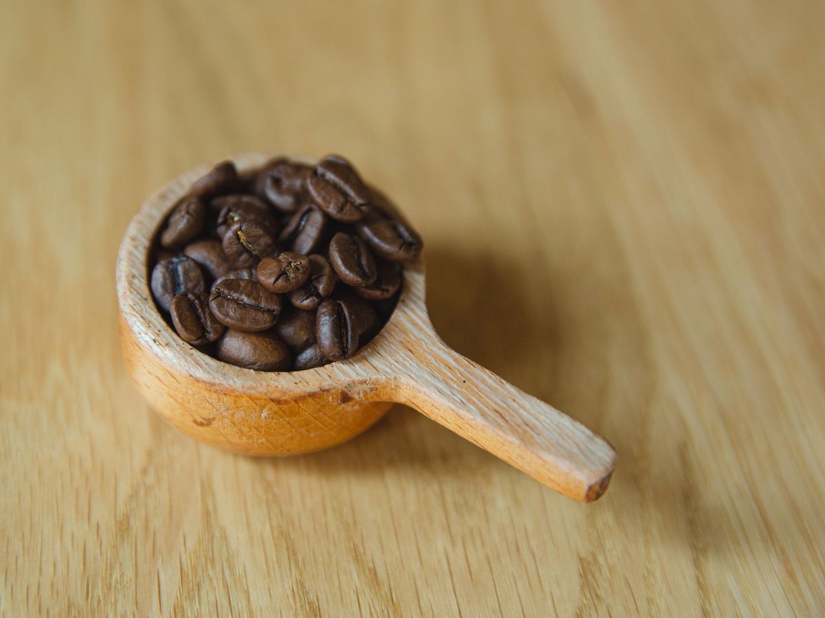 A wooden spoon full of roasted coffee beans on a wooden surface